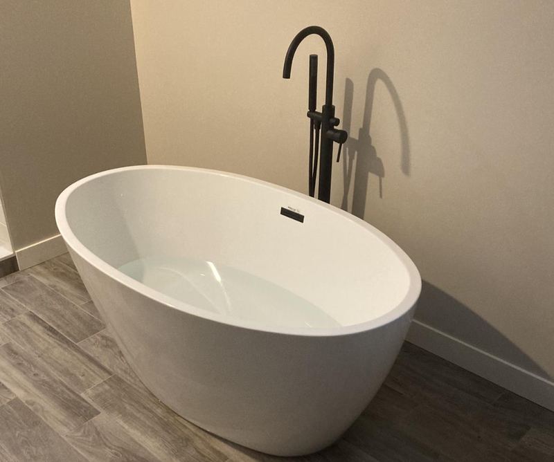 White freestanding oval soaking tub with a matte black floor-mounted tub filler and hand shower.