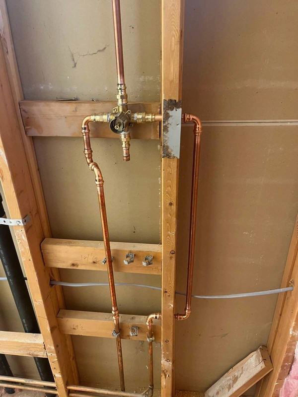 New copper water piping roughed in with a brass valve inside an open wood stud wall.