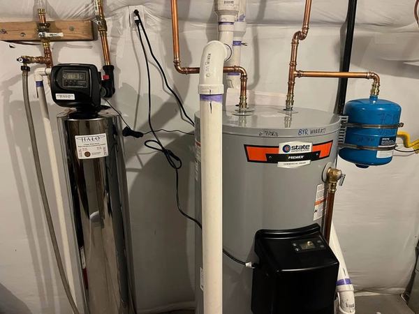 Stainless steel whole-home filtration tank next to a newly installed tank water heater with a blue expansion tank.
