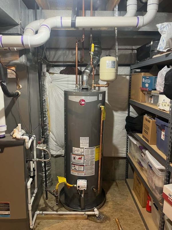 Tank water heater in a basement with white PVC vent piping overhead and an expansion tank above it.